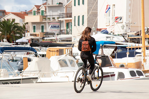 Vodice, Croatia - September 1, 2020: Young woman riding a bike on the dock promenade in Mediterranean town by the sea