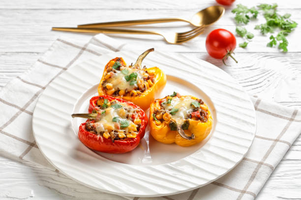 stuffed bell peppers with ground beef, corn and cheese classic stuffed bell peppers with ground beef, corn and cheese on a white plate on a wooden table with golden cutlery, horizontal view from above, close-up hungarian pepper stock pictures, royalty-free photos & images