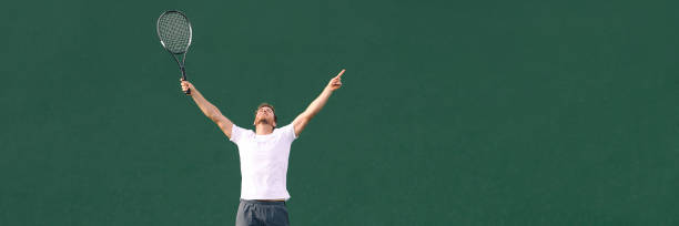 jugador de tenis ganar animando celebrando la victoria en el punto de partido. ganador atleta masculino feliz con los brazos hasta el cielo en la celebración del éxito y ganar. bandera panorámica. - cheering men t shirt celebration fotografías e imágenes de stock