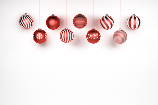 Red and white Christmas Baubles with different designs hanging in front of a white stone background. Copyspace.