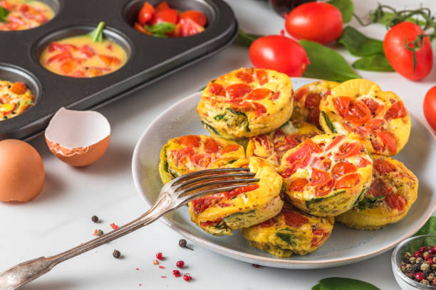 istock Egg muffin cups or omelet with spinach and tomatoes in a plate and in muffin tin with forkl. cooking concept 1272451179