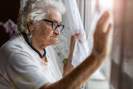 Mujer mayor mirando por la ventana en casa photo