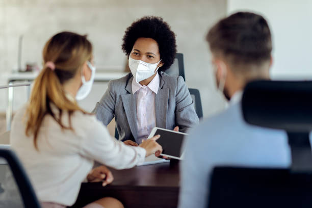 istock African American financial advisor and her clients using digital tablet while wearing protective face masks during the meeting. 1272458772