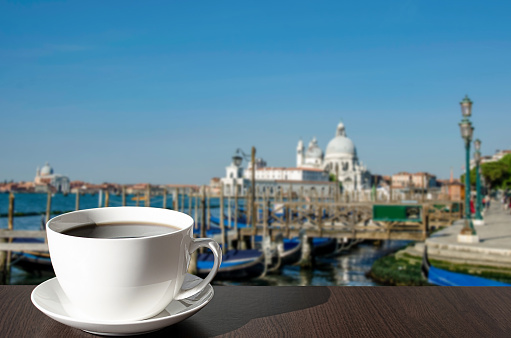 Cup of coffee on the table with view on gondolas and church in Venice, Italy