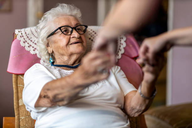 weibliche heimpflegerin unterstützt alte frau, um vom sessel im pflegeheim aufzustehen - demenz stock-fotos und bilder