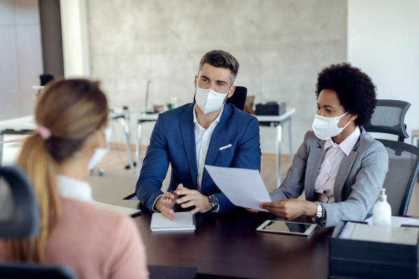 Business coworkers wearing face masks while talking to potential job candidate in the office. Members of human resource team wearing protective face masks while communicating with a candidate during job interview in the office. kn95 face mask photos stock pictures, royalty-free photos & images