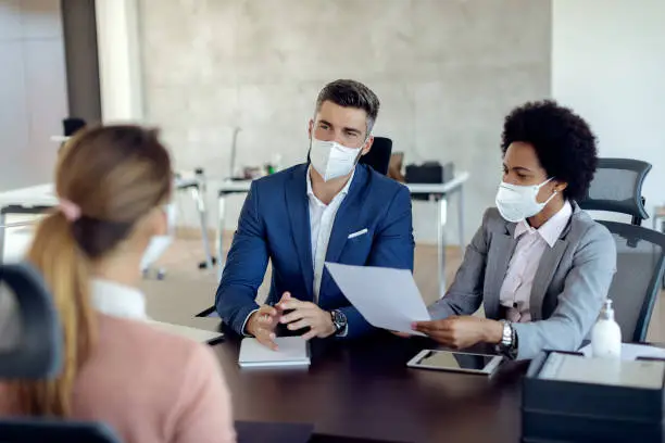 Photo of Business coworkers wearing face masks while talking to potential job candidate in the office.