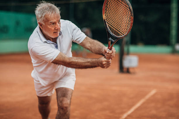 Senior man playing tennis One man, senior man tennis player on tennis court, playing tennis. backhand stroke stock pictures, royalty-free photos & images