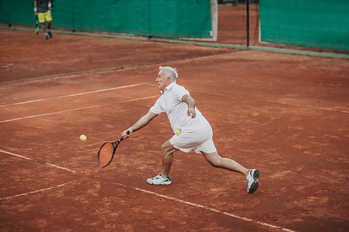 Active senior man playing tennis on the outdoor tennis court. Concept of healthy and fit senior people.