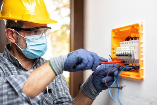 Electrician at work with face protected by surgical mask to prevent Coronavirus infection. Covid-19 pandemic. Electrician at work on an electrical panel protected by helmet, safety goggles and gloves; wear the surgical mask to prevent the spread of Coronavirus. Construction industry. Covid-19 Prevention. repairing electrical component stock pictures, royalty-free photos & images