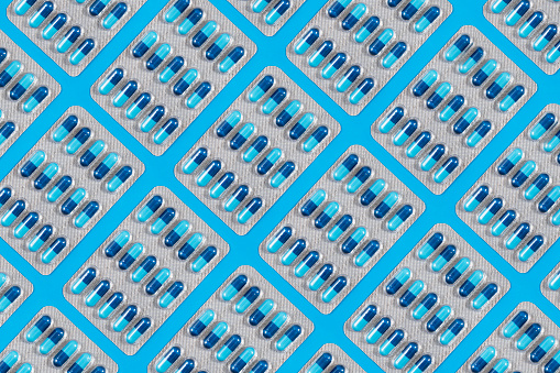 Medicine capsules in blister packs on blue background with copy space