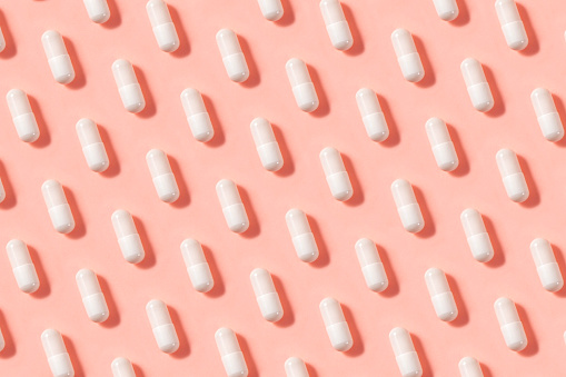 White pills on soft pink background
