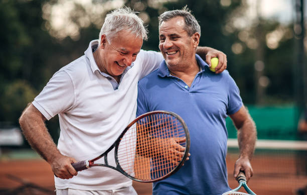 zwei aktive senioren sprechen beim gehen auf dem tennisplatz - tennis active seniors healthy lifestyle senior men stock-fotos und bilder