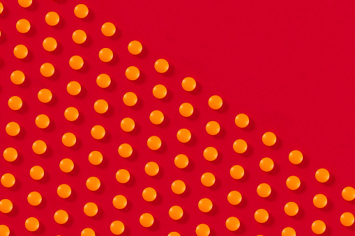 Orange colored pills flat lay on red background with copy space