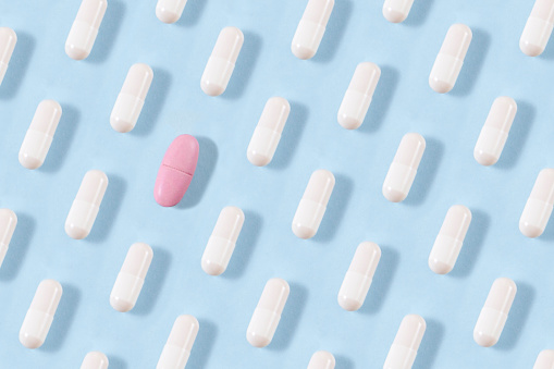White pills arrangement on soft blue background with one pink pill standing out from them