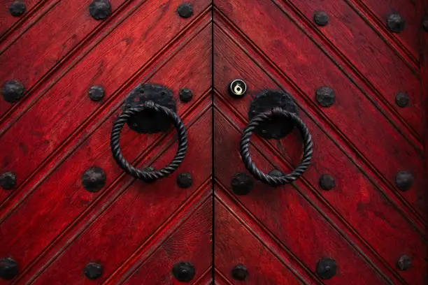 Photo of Authentic red wooden front door of an old european house. Closeup photo of the decorated door`s knobs made in the form of a ring and keyhole.