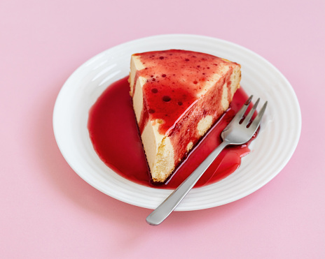 Cheesecake on a white plate with strawberry sauce, on a light pink background.