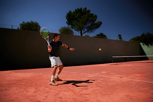 Young adult male tennis player playing match on clay court