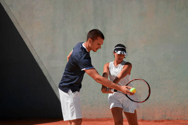 Tennis instructor giving lessons to young woman in tennis clay court stock photo