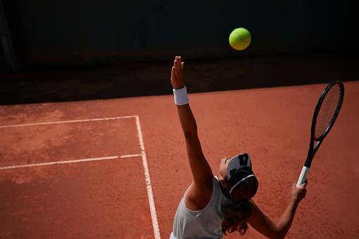 Professional female tennis player serving ball during match on clay court