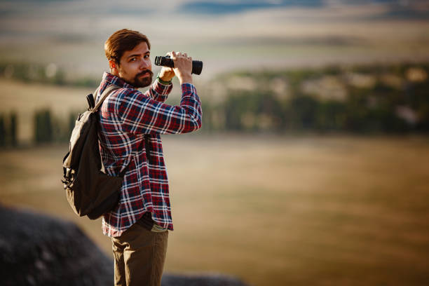 un tipo mirando binoculares en la colina. hombre en camiseta con mochila - pursuit binoculars mountain sky fotografías e imágenes de stock