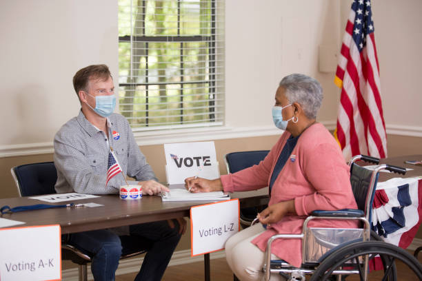 Vote Polling Place Workers at local Polling Place helping voters.  They wear protective face masks.  Voter is in a wheelchair. voter registration photos stock pictures, royalty-free photos & images