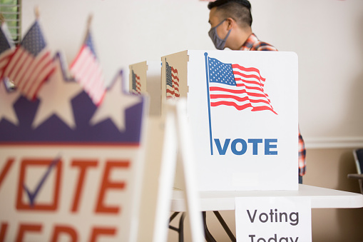 Voters at Polling Place casting their ballots.  Voter Here sign in foreground.