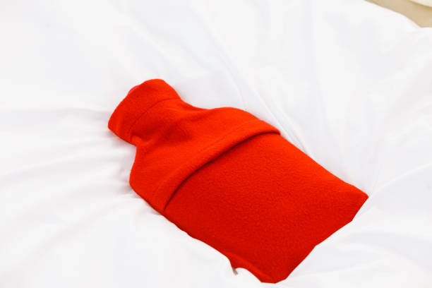 istock Warm red hot water bottle on white bedding 1272474008