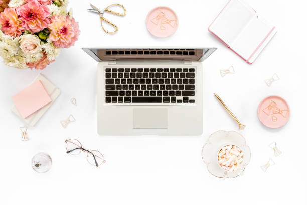 Stylized women's home office desk. Workspace with laptop, computer, bouquet ranunculus and roses, clipboard on white background. Flat lay. Top view