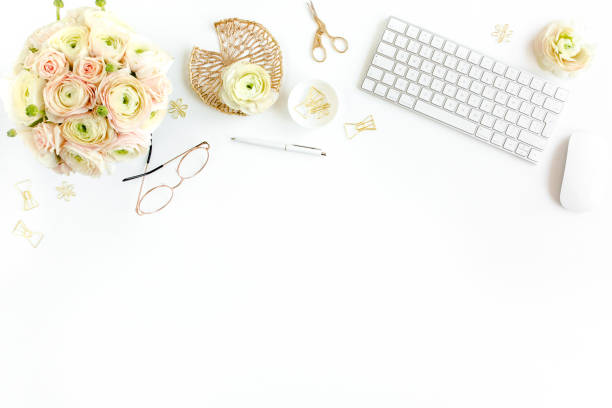 istock Stylized women's home office desk. Workspace with computer, bouquet ranunculus and roses, clipboard on white background. Flat lay. Top view 1272476070