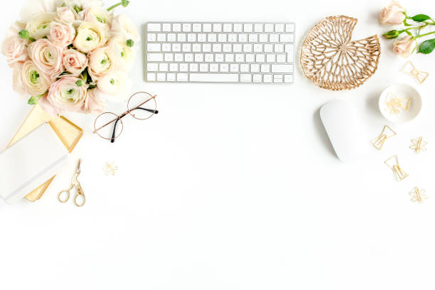 istock Stylized women's home office desk. Workspace with computer, bouquet ranunculus and roses, clipboard on white background. Flat lay. Top view 1272476759