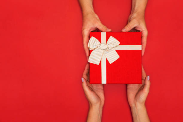 hombre dando caja de regalo roja con cinta de oro a la mujer sobre fondo rojo. vista superior. regalo para cumpleaños, san valentín, navidad o año nuevo. - box men holding isolated fotografías e imágenes de stock