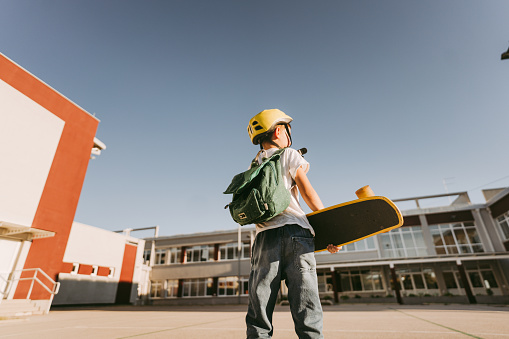 Photo of a skater boy holding his skateboard and spending some time in the schoolyard before entering school.