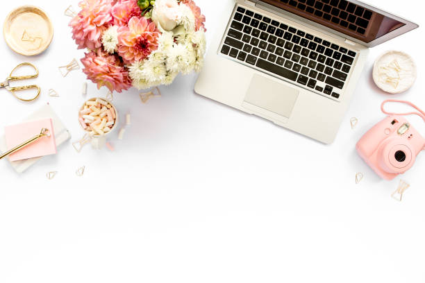 istock Stylized women's home office desk. Workspace with laptop, computer, bouquet ranunculus and roses, clipboard on white background. Flat lay. Top view 1272480667