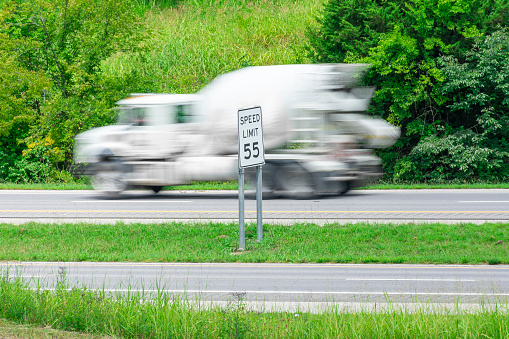 Horizontal shot of a speeding concrete truck streaking by a speed limit sign.  Blurring shows motion.