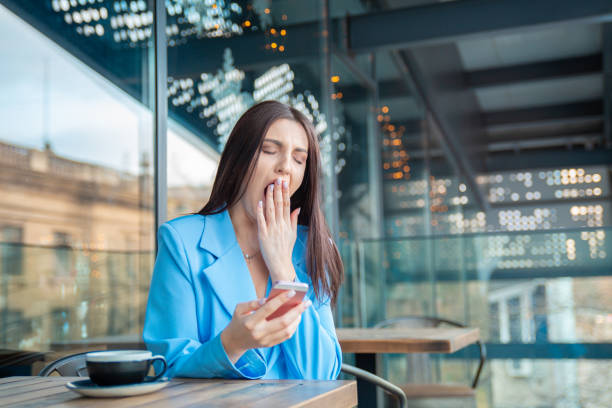 donna stanca annoiata e sbadigliante mentre lavora al telefono sul balcone - yawning women drink coffee cup foto e immagini stock