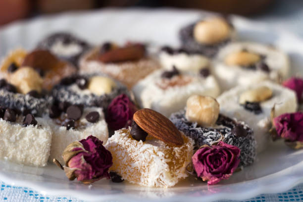 istock Assorted Turkish delight on a white plate. Traditional yellow, white and black sweets with nuts, dried roses ornaments. Goodies 1272481042