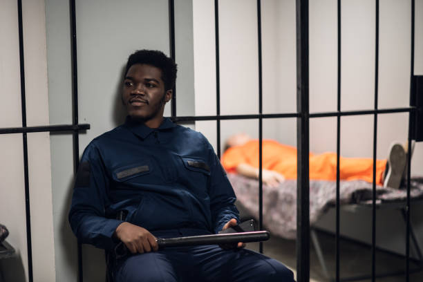 a strong black prison guard guards the cells with prisoners in the prison corridor - prison cell imagens e fotografias de stock