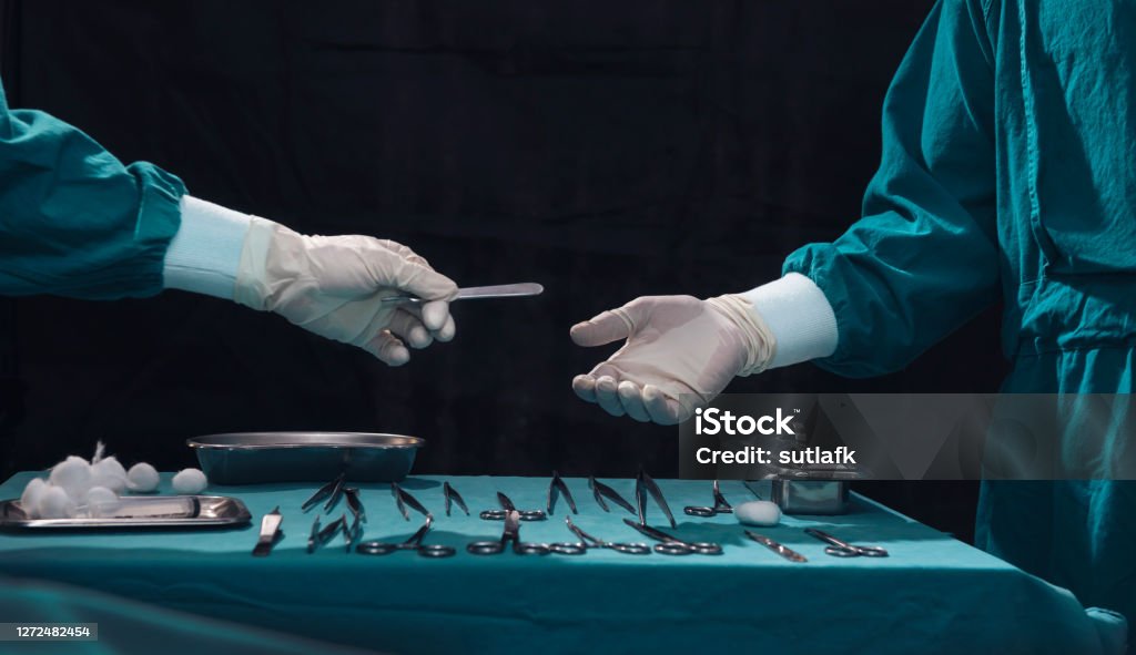 Surgery team operating in a surgical room.Assistant passing surgical scalpel to the doctor. Surgery team operating in a surgical room.Assistant passing surgical scalpel to the doctor. Hand of doctor in white glove. Two surgeons working and passing surgical equipment in the operating room Surgeon Stock Photo