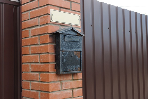 one black iron mailbox on a brown brick wall and a metal fence