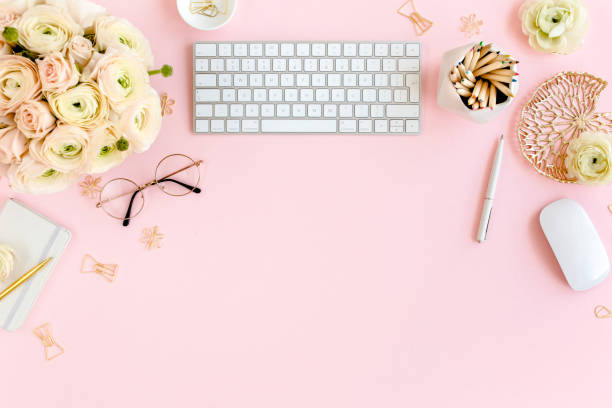 istock Stylized, pink women's home office desk. Workspace with computer, bouquet ranunculus and roses, clipboard on pink background. Flat lay. Top view 1272484625