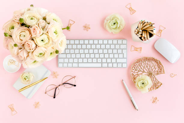istock Stylized, pink women's home office desk. Workspace with computer, bouquet ranunculus and roses, clipboard on pink background. Flat lay. Top view 1272484765