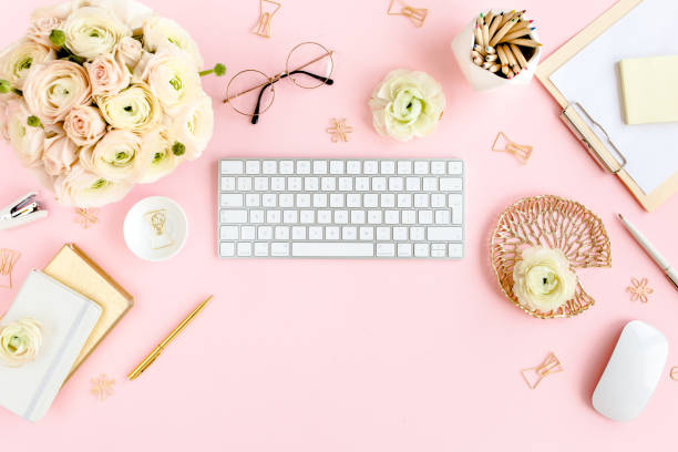 istock Stylized, pink women's home office desk. Workspace with computer, bouquet ranunculus and roses, clipboard on pink background. Flat lay. Top view 1272484941