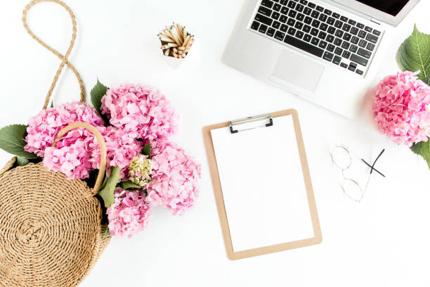 istock Stylized women's desk. Workspace with clipboard, laptop, bouquet hydrangea, accessories on white background. Flat lay. Top view 1272485124
