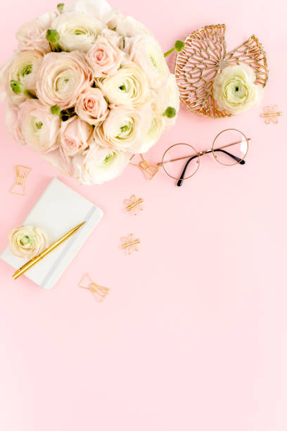 istock Stylized, pink women's home office desk. Workspace with bouquet ranunculus and roses, clipboard on pink background. Flat lay. Top view 1272485748