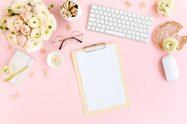 istock Stylized, pink women's home office desk. Workspace with computer, bouquet ranunculus and roses, clipboard on pink background. Flat lay. Top view 1272485783