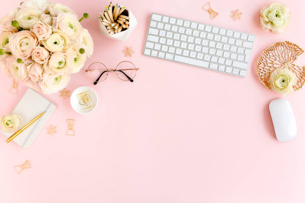 istock Stylized, pink women's home office desk. Workspace with computer, bouquet ranunculus and roses, clipboard on pink background. Flat lay. Top view 1272485933
