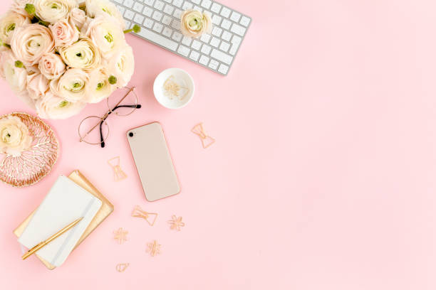 istock Stylized, pink women's home office desk. Workspace with computer, bouquet ranunculus and roses, phone on pink background. Flat lay. Top view 1272486097