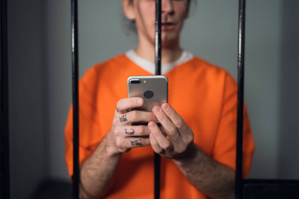 a dangerous criminal with tattoos on his face in prison got a smartphone to commit cyber crimes over the internet - prison cell imagens e fotografias de stock