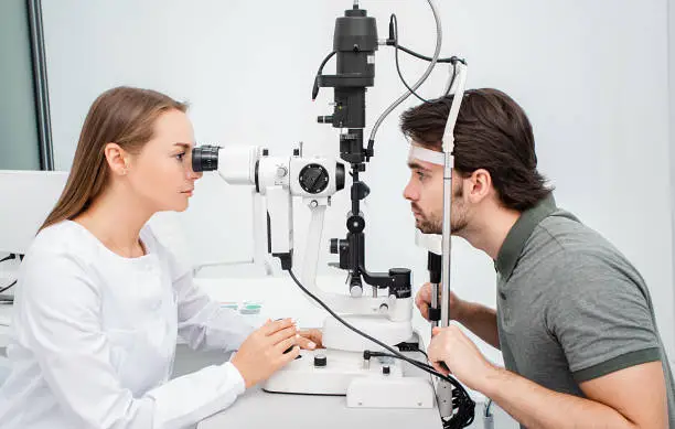 Optometrist woman using a binocular slit-lamp examines the eye of an adult man patient